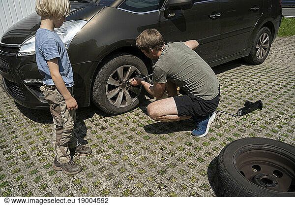 Boy watching father repairing car tire in yard