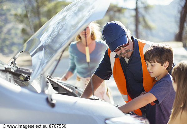 Boy watching roadside mechanic check car engine