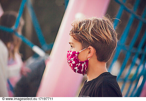 Boy wearing a mask playing alone at a pink playground