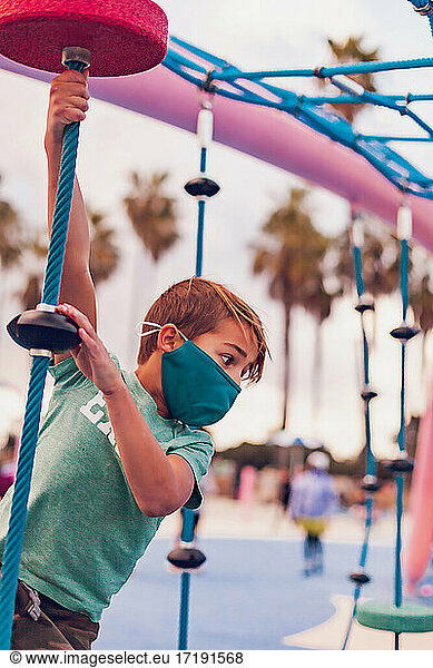 Boy wearing a mask playing alone at a playground - hanging.