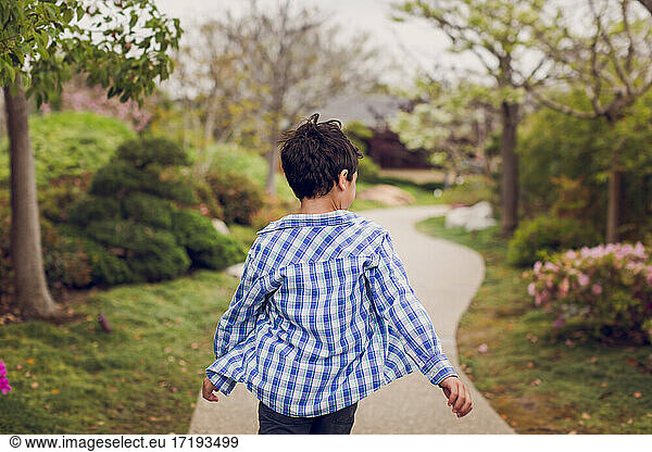 Boy wearing a plaid shirt walking on a path.