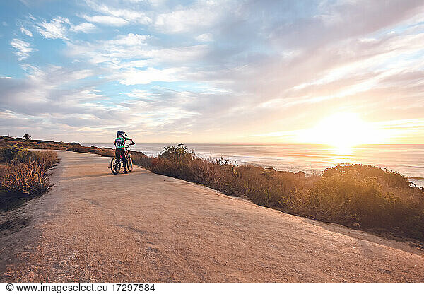 Boy wearing a tie-dye shirt rides his bike on a coastal trail.