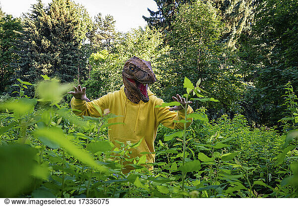 Boy wearing dinosaur mask while scaring amidst plants