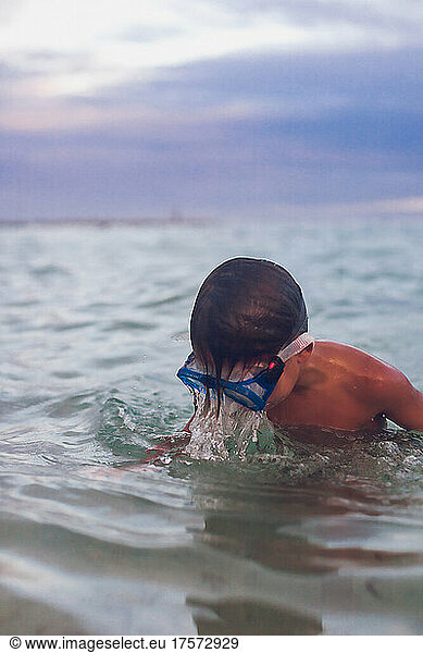 Boy wearing goggles playing in the ocean in Mexico.