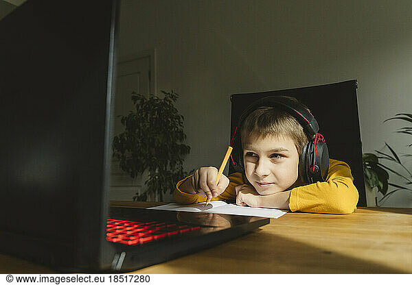 Boy wearing headset studying online through laptop at home