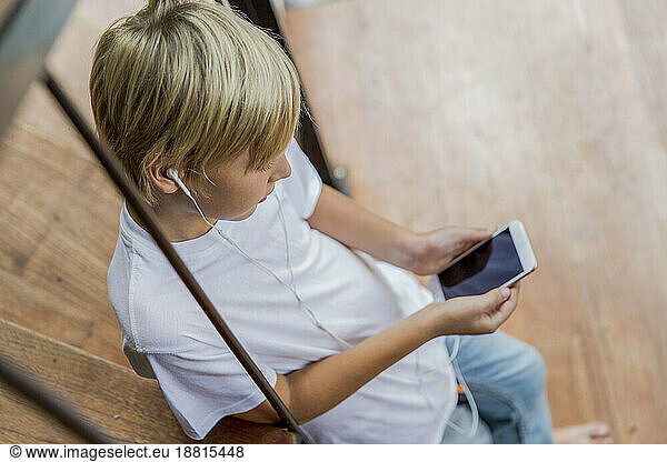 Boy wearing in-ear headphones using smart phone at home