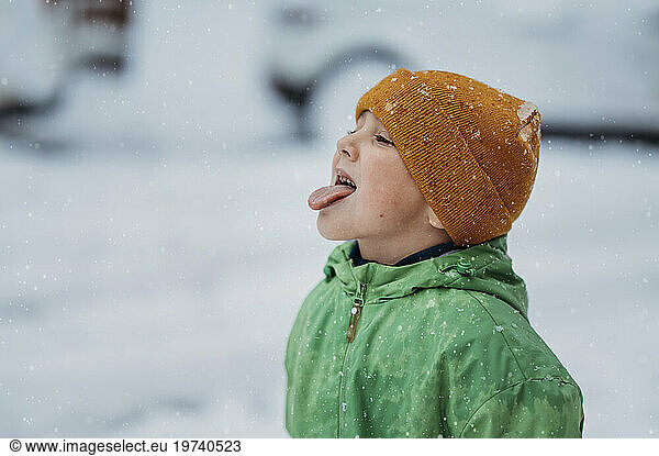 Boy wearing knit hat catching snow on tongue in winter