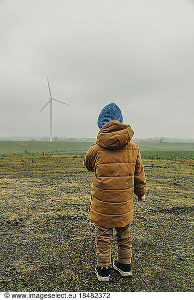 Boy wearing knit hat looking at wind turbine