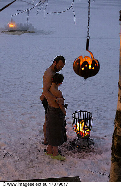 Boy wearing towel standing with father by bonfire at night