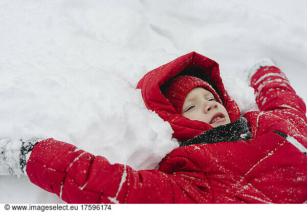 Boy wearing warm clothing lying on snow in winter