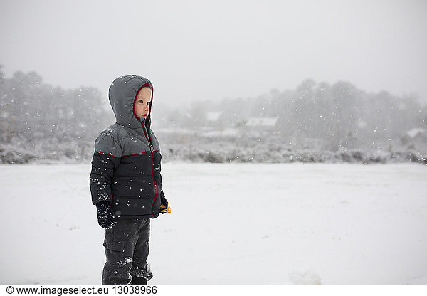 Boy wearing warm clothing while standing on snowy field during snowfall