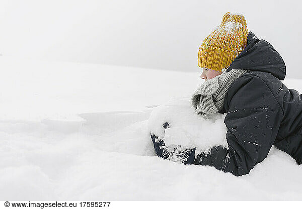 Boy wearing yellow knit hat playing with snow