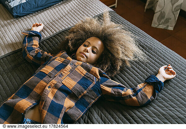 Boy with Afro hairstyle lying on bed at home