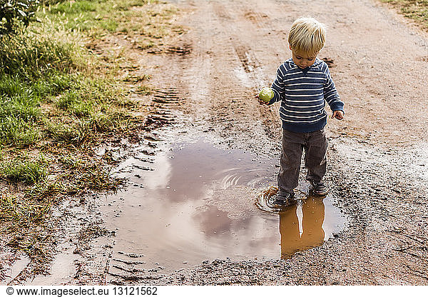 Boy with apple standing in dirty puddle