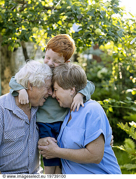 Boy with arms around grandparents in garden