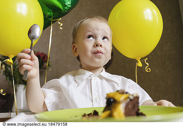 Boy with balloons and cake celebrating birthday at home