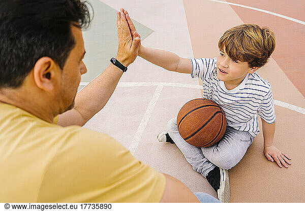 Boy with basketball giving high five to man at sports court
