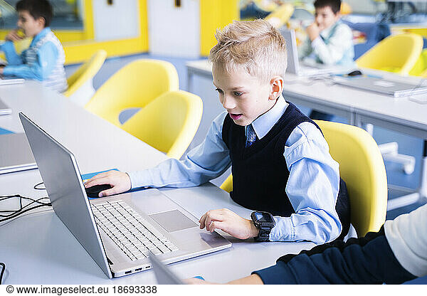 Boy with blond hair using laptop sitting in computer class