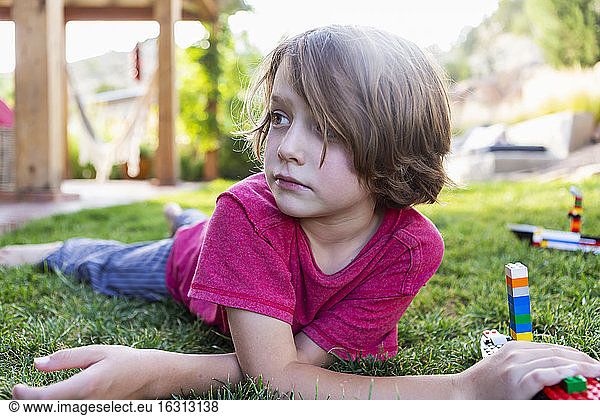 Boy with brown hair lying on lawn  playing with building blocks.