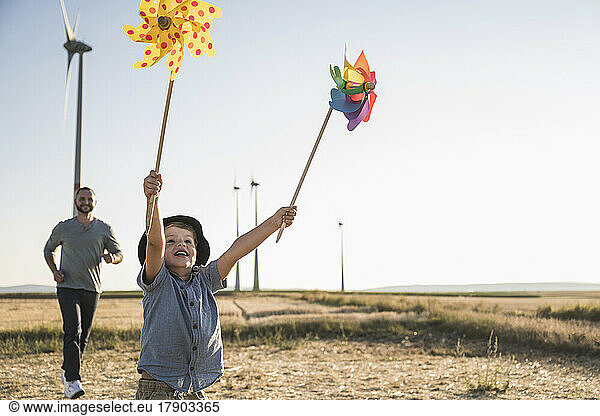 Boy with colorful pinwheels running in windpark with father following