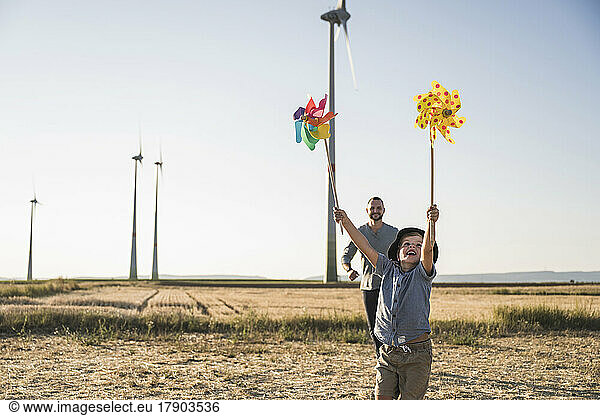 Boy with colorful pinwheels running in windpark with father following