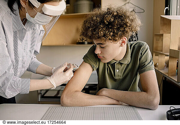 Boy with curly brown hair looking at nurse injecting medicine at home
