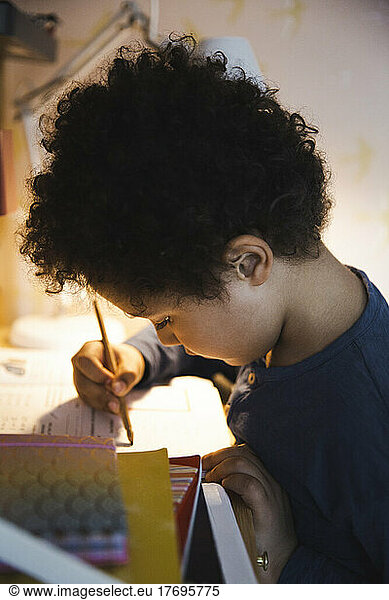 Boy with curly hair doing homework while writing in book