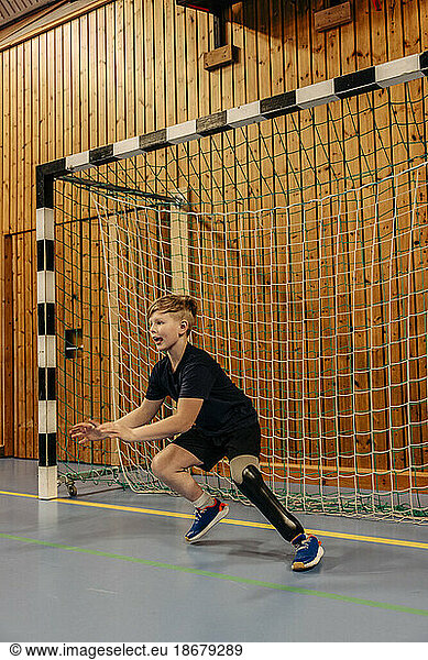 Boy with disability goalkeeping near net while playing football at sports court