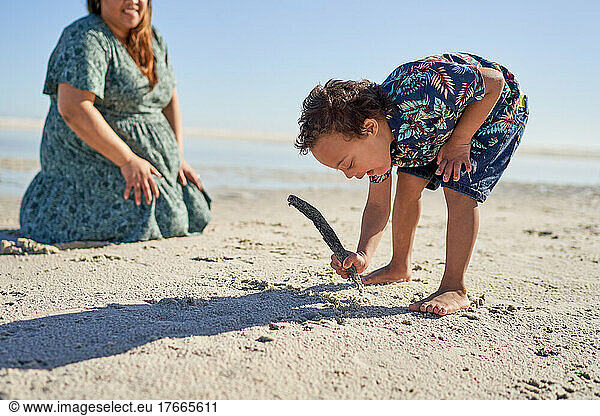 Boy with Down Syndrome drawing in sand with stick on sunny beach
