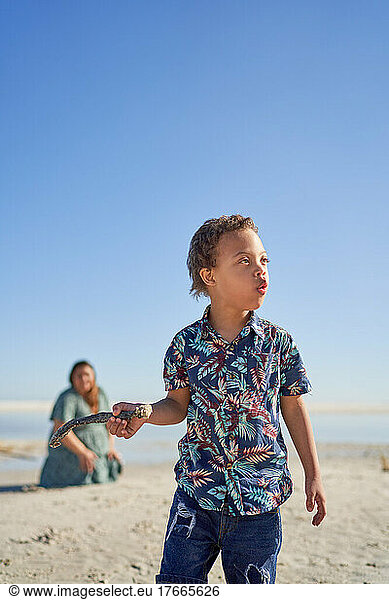 Boy with Down Syndrome holding stick on sunny beach