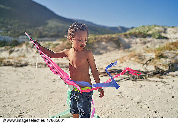 Boy with Down Syndrome in denim shorts playing with kite on beach