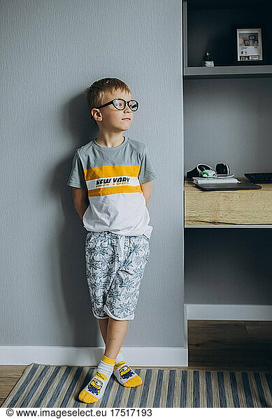boy with glasses stands near the wall