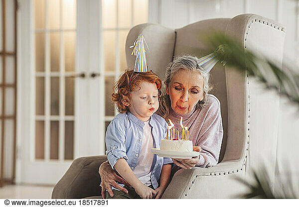 Boy with grandmother blowing candles on birthday cake at home