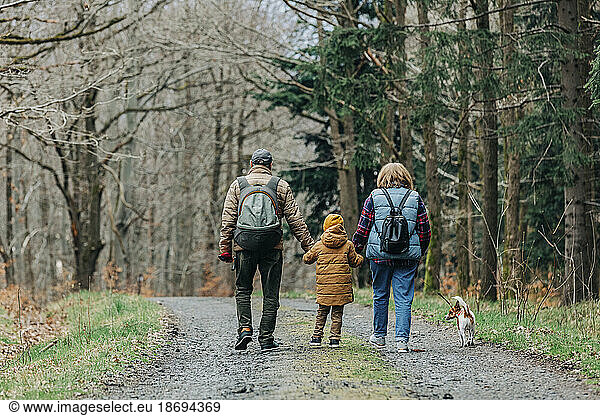 Boy with grandparents and dog walking on footpath in forest