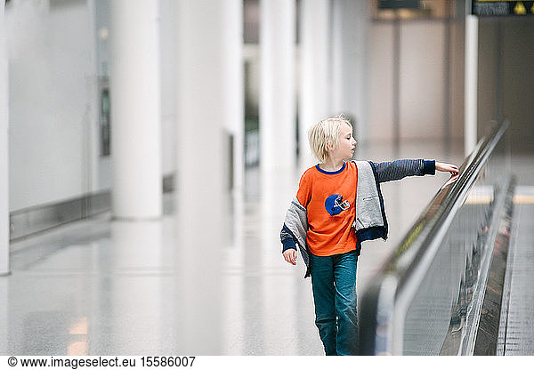 Boy with hand on handrail of moving walkway in airport  selective focus