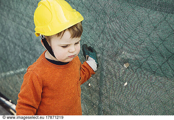 Boy with hard hat standing by fence