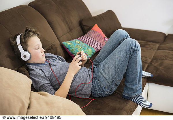 Boy with headphones and smartphone on couch