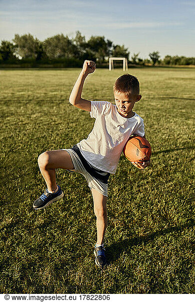 Boy with rugby ball doing haka dance standing on one leg at sports field