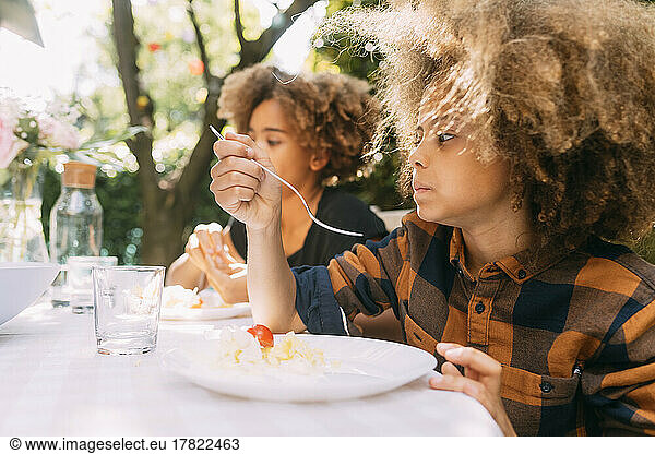 Boy with sister eating lunch at dining table in yard