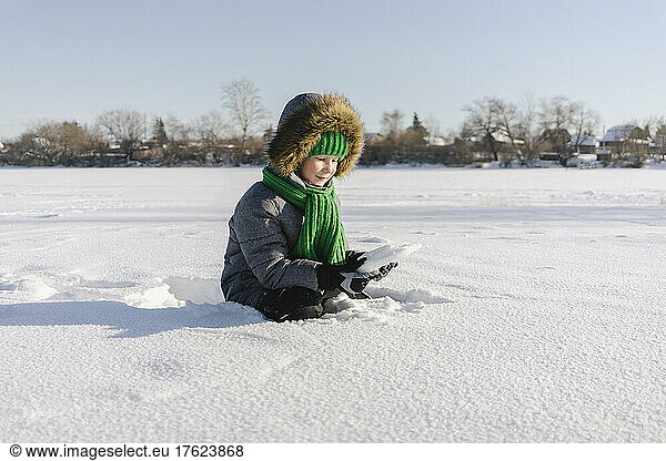 Boy with warm clothing sitting in snow