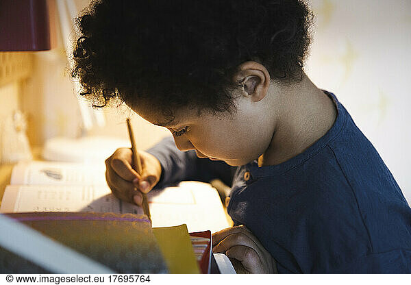 Boy writing in book while doing homework
