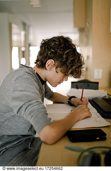 Boy writing in book while doing homework sitting at table