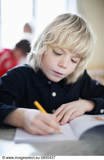 Boy writing in book with friend in the background