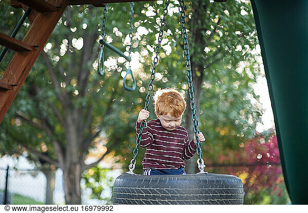 Boy 3-4 years old looking down while swinging on tire swing outdoors