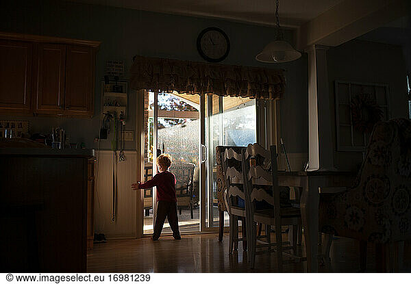 Boy 3-4 years old opening door in kitchen in pretty light and shadows