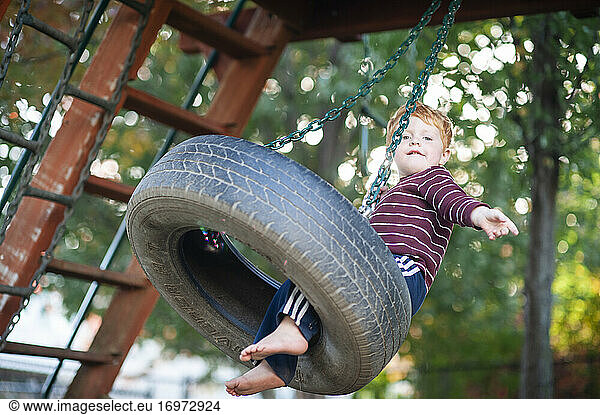 Boy 3-4 years old swinging on tire swing in backyard during fall