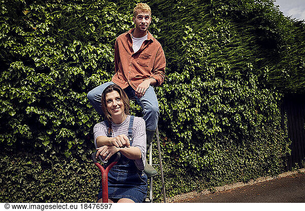 Boyfriend and girlfriend sitting on ladder near hedge