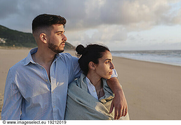 Boyfriend with arm around girlfriend on beach at sunset