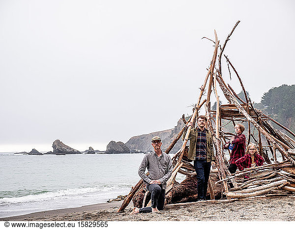 Boys and men standing in driftwood structure on a California beach