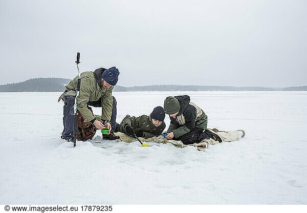 Boys doing fishing by mature man at frozen lake